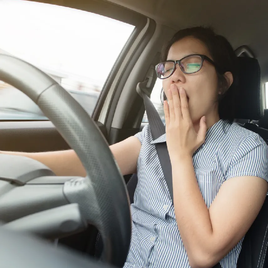 一名女性駕駛在汽車內因嚴重睡眠不足而張口打哈欠，眼神顯露疲態，展示了微睡眠入侵前常見的神經疲勞與生理崩潰訊號。